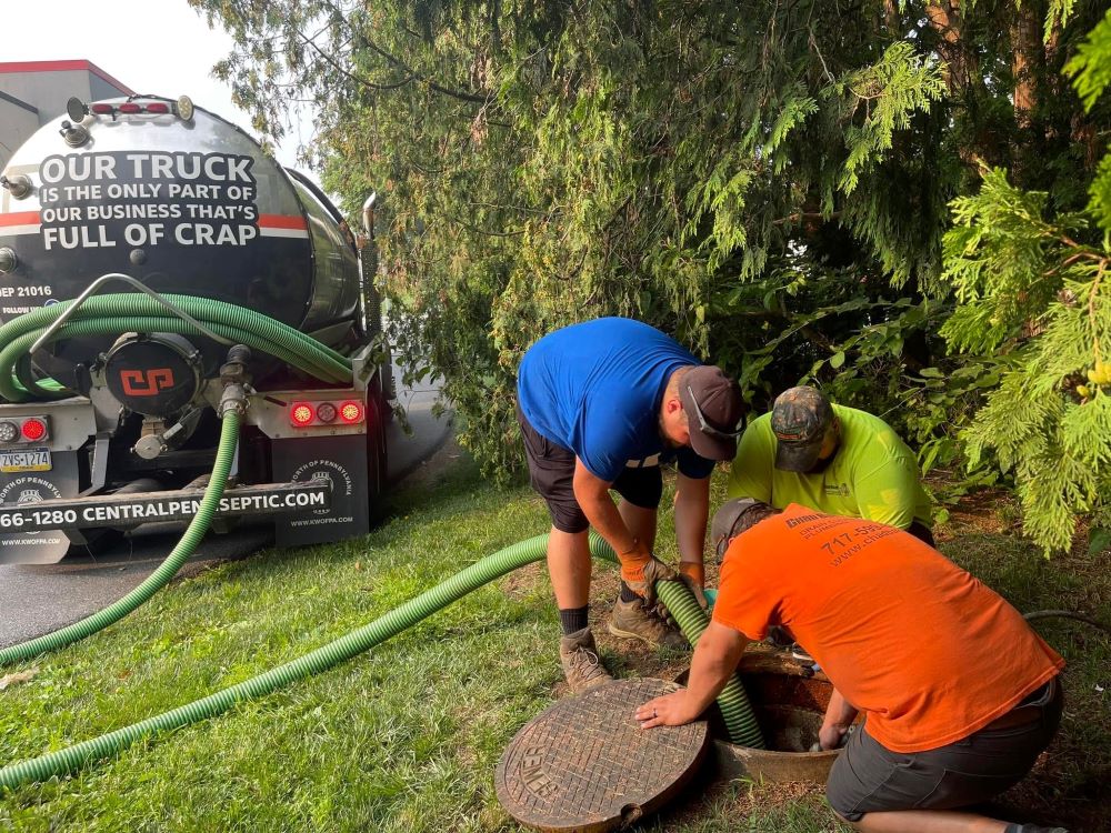 Three men from Central Penn Septic are repairing a sewer pipe together in a construction site.